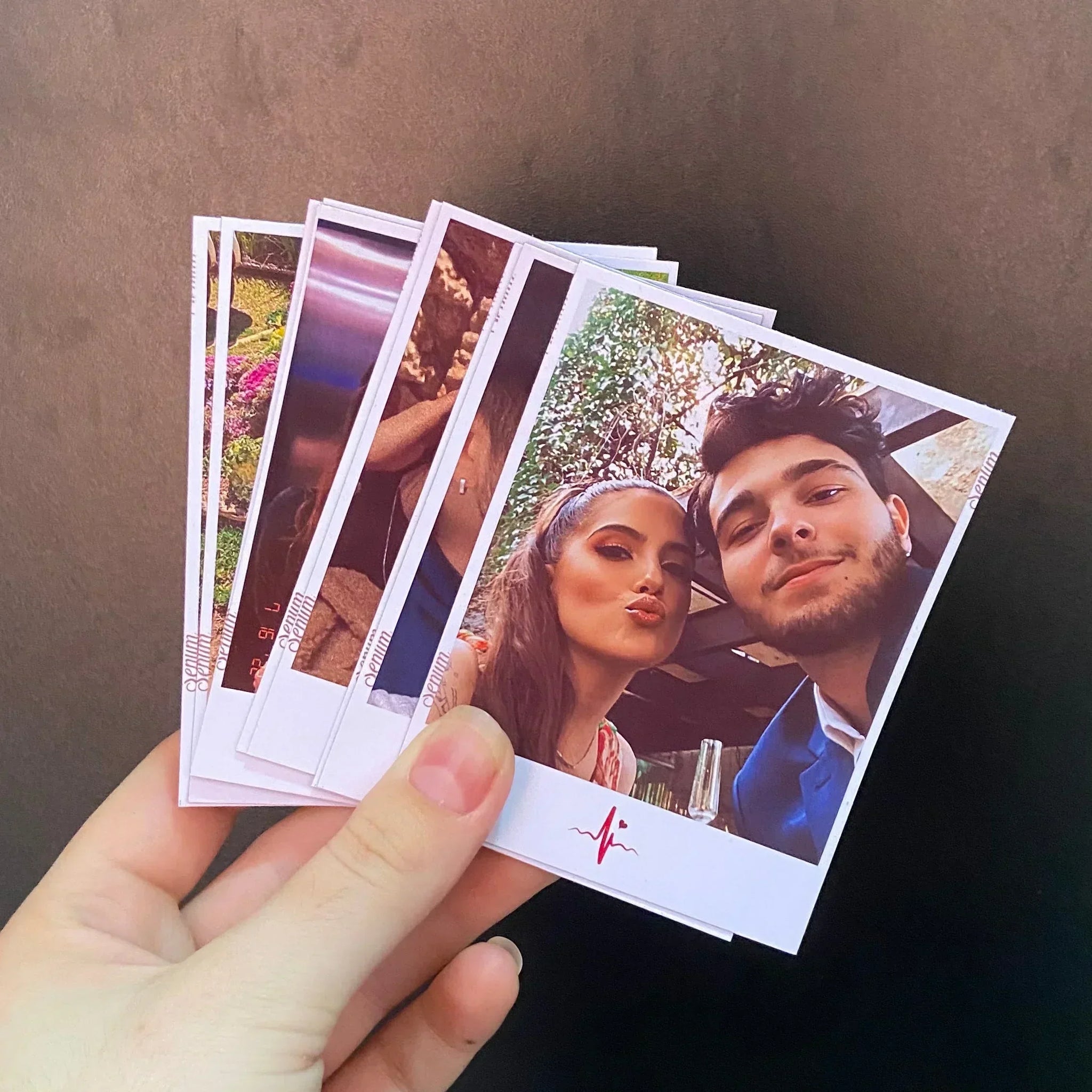 Mão segurando várias fotos instantâneas de casal sorrindo, fundo preto, impressão personalizada.