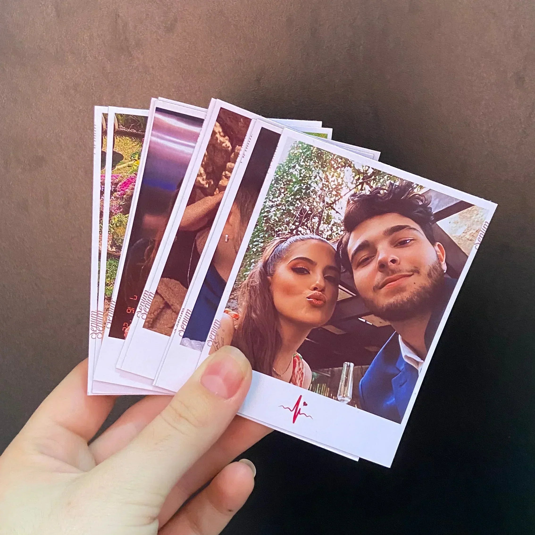 Mão segurando várias fotos instantâneas de casal sorrindo, fundo preto, impressão personalizada.
