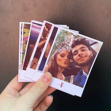 Mão segurando várias fotos instantâneas de casal sorrindo, fundo preto, impressão personalizada.