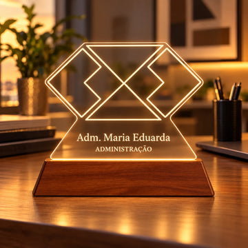 Luminária Administração personalizada acesa, com símbolo geométrico da Administração e o nome Adm. Maria Eduarda gravados em acrílico sobre base de madeira