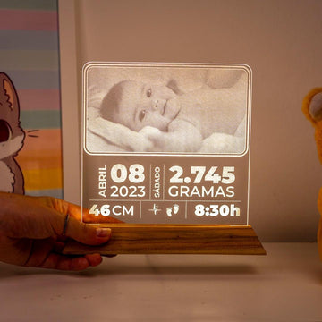 Luminária personalizada com foto de bebê, dados de nascimento e base de madeira em ambiente infantil.