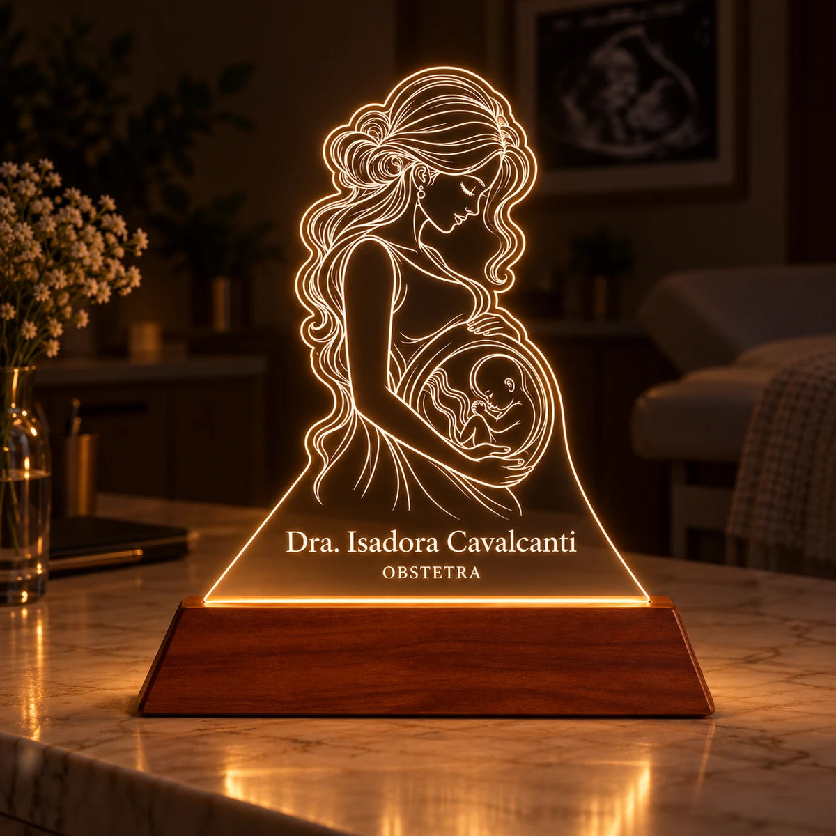 Luminária Obstetra acesa em ambiente de consultório com luz baixa, desenho de gestante e bebê brilhando em branco quente sobre a base de madeira
